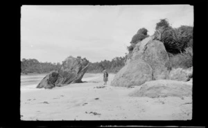 Alice Williams walking on a beach with large rocks and bush behind, Stewart Island, (Rakiura)