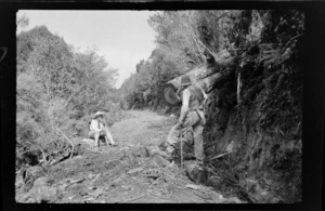 William Williams looking at fallen tree with Alice Williams sitting down on a bush track, Stewart Island (Rakiura)