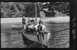 Group of unidentified people aboard a boat with beach, trees, boat shed and buildings in the background, Stewart Island (Rakiura)