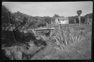 William Williams walking over a bridge, with hut in the background, Stewart Island (Rakiura)