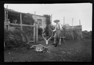 Alice Williams with a stag skull and rifle beside house, Stewart Island (Rakiura)