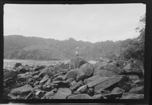 Alice Williams standing on a large rock, with the beach and hills behind, Stewart Island (Rakiura)