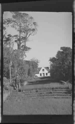 Alice Williams with possibly Edgar Williams standing on steps leading to a two storey house, Stewart Island (Rakiura)
