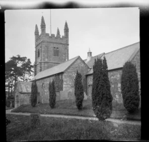 An unidentified country stone block church and turreted bell tower with flag pole surrounded by trees and fields, Wales