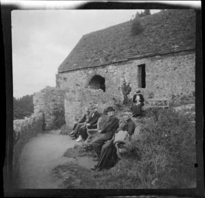 Group seated outside a stone cottage, all unidentified except for Lydia Williams, at front, probably Devon, England