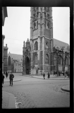 Church with bell tower on corner of cobblestone streets, and an [artist?] selling works outside, Rouen, France