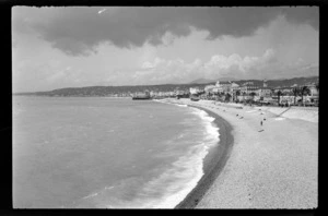 View along beach, with sea pier [domed?] building, Nice Opera House, multi-storey buildings and palm trees, Nice, France