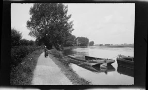 Lydia Williams standing on a path beside two barges on the [Oxford?] canal system with trees beyond, [Oxfordshire?], England