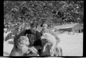 Unidentified man and woman, sitting on kennel with two huskies, Mount Cook area