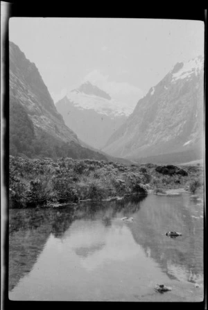 View over water [lake? tarn?] to mountains, between Howden Hut and Homer Hut, Southland Region
