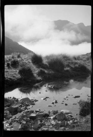 Stream, tussocks and clouds partially covering mountains in background, Greenstone ford, Fiordland National Park, Southland