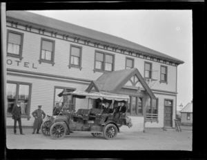 A service car parked outside a large two-storied wooden hotel, including unidentified passengers and driver, Hamner Springs, Hurunui district, Canterbury region