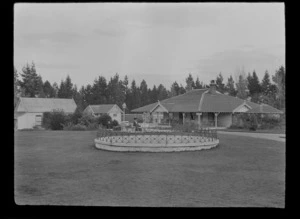 Lydia Williams sitting on a park bench with bath house in the background, Hanmer Springs, Canterbury Region