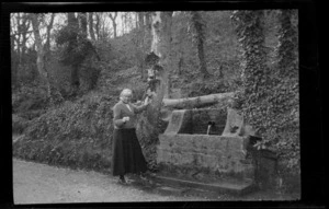 Lydia Williams drinking water from an old spring stone well and trough, Brittany, France