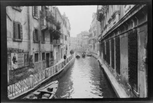 Buildings on either side of canal with gondola rowing between two stationary gondolas, Venice, Italy