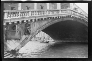 A gondolier by a stone bridge, with plaque and statue visible on side of bridge, Venice, Italy