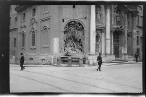 Street scene including building alcove with statue of man lying next to tree, other alcoves with statues on front of building and people walking on street, unknown location, Rome, Italy