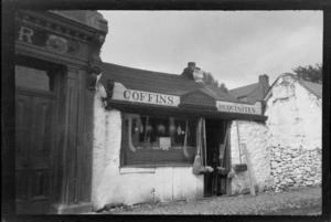 Coffins and undertakers store belonging to P O'Shea, including brooms hanging outside of doorway and hurley, sliotar, [footballs and possibly hand pumps?] displayed in shop window, Killarney, County Kerry, Ireland