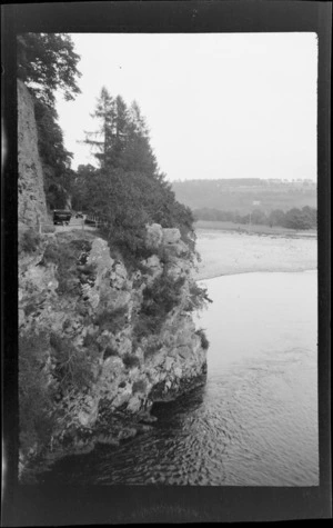 Vehicles on road at top of rocky bluff with [loch or river] below, Scotland