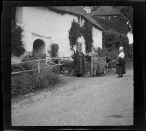 A man and two women, all unidentified, standing outside a thatched cottage, [Bovey?] Devon, England