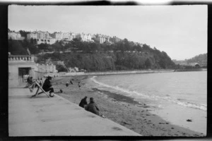 Torre Abbey Sands, Torquay, South Devon, England, showing holidaymakers in deckchairs on promenade and beach, and buildings on bluff overlooking sea