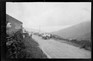 Row of six cars stopped on road by house, including hills in the background, Lake District, England, United Kingdom
