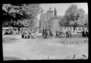 Cathedral Square, Christchurch City, Canterbury, showing people sitting around base of statue of John Robert Godley, with Chief Post Office in background