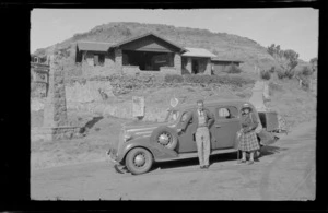 An unidentified man and woman standing by a motorcar, on road in front of the Sign of the Kiwi rest house, junction of Summit Road and Dyers Pass Road, Heathcote Valley, Canterbury region