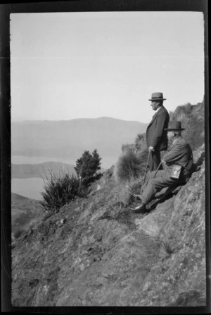 Two unidentified men sitting on a hillside, looking towards [Lyttelton?] harbour, [Port Hills, Canterbury region?]