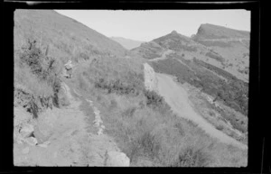 Hillside track, including an unidentified woman walking in middle distance, [Port Hills, Canterbury region?]