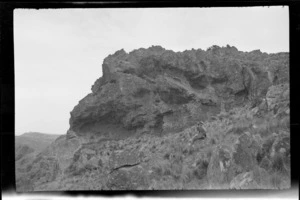 Rocky outcrop, with an unidentified woman sitting on hill alongside, [Port Hills, Canterbury region?]