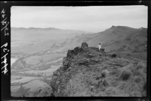 Woman sitting on rocky hilltop, [Heathcote Valley, Canterbury region?]