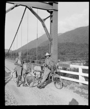 Two unidentified men with bicycles, on suspension bridge over Fox River, Buller District, West Coast Region