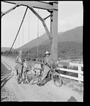 Two inidentified men with bicycles, on a suspension bridge over Fox River, Buller District, West Coast Region
