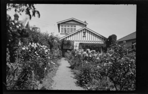 View up garden path bordered by roses to two-storied house, location unidentified