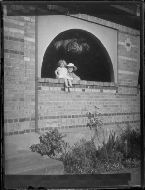 An unidentified woman and small child sitting in an arched window in a brick wall, at Westport Technical High School, West Coast Region