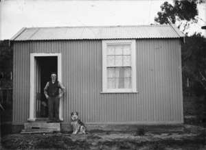 Elderly man and dog alongside a corrugated iron dwelling