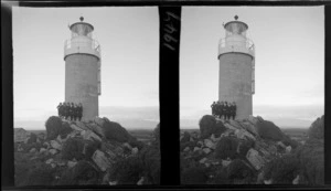 Group of unidentified schoolgirls from Westport Technical High School, standing against base of lighthouse, Cape Foulwind, Buller District, West Coast Region