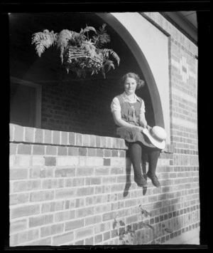 An unidentified schoolgirl sitting in an arched opening in a brick wall, at Westport Technical High School, West Coast Region