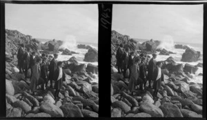 Group of unidentified schoolgirls from Westport Technical High School, standing on boulders next to sea, Cape Foulwind, Buller District, West Coast Region