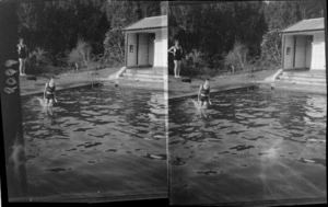 Two unidentified girls jumping from diving board into an outdoor swimming pool, [Waikato Region?]