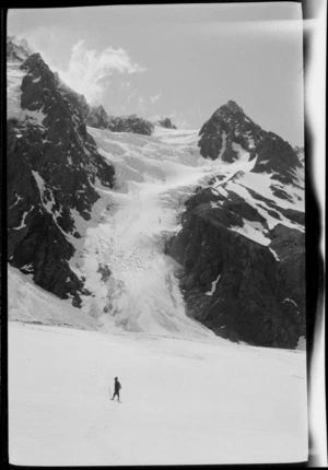 Distant figure crossing snow-covered plane in mountains, [West Coast Region]