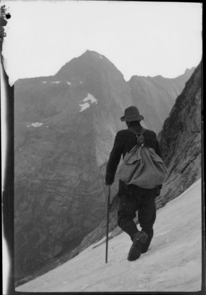 An unidentified mountaineer wearing a pack, walking on a snow-covered slope, [Fiordland National Park]