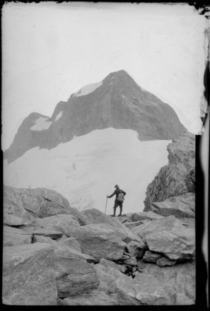 [Jack Murrell?] standing on boulders with peak [and glacier?] beyond, [Fiordland National Park?]