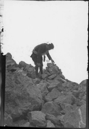 An unidentified mountaineer wearing a rope, putting stones on a cairn, [Canterbury Region or Southland District?]