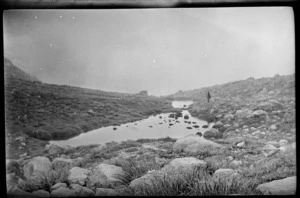 Stream through alpine grasslands, with distant figure, misty mountain beyond, [Canterbury, Otago or Southland?]