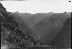 View from grassy slope down into valley surrounded by mountains, [West Coast Region]