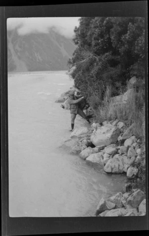 A man [Tracy Thomas Gough?] wading in river in mountain valley, Canterbury Region