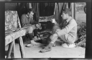 Edgar Williams, right, and another man [Tracy Thomas Gough?], drinking from mugs in front of a fireplace in a mountain hut, Southern Alps, Canterbury Region