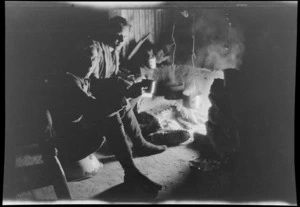 Edgar Williams, left, an another man [Tracy Thomas Gough?], sitting in front of a fireplace at night, in a mountain hut, Southern Alps, Canterbury Region